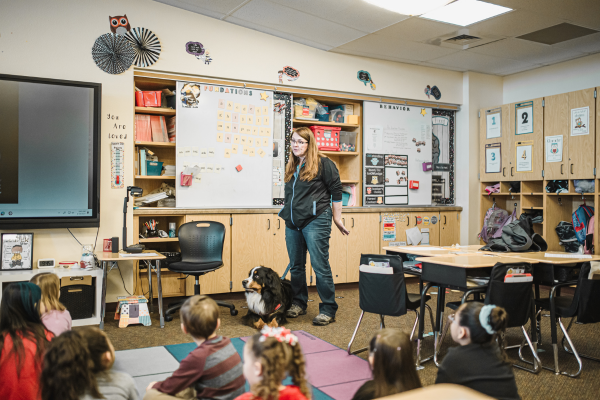 A woman with a service dog and an invisible disability talking to a group of students